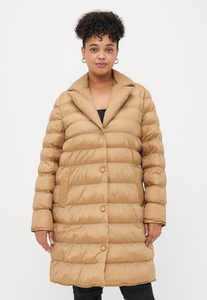 Beige pufferjakke med krage, knappeåpning og horisontal quiltet mønster. Har sidelommer og er midt på låret i lengden.