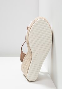 Sandale à talon compensé avec plateforme en jute tissée, semelle en caoutchouc blanc avec rainures horizontales et bride de cheville en cuir marron.