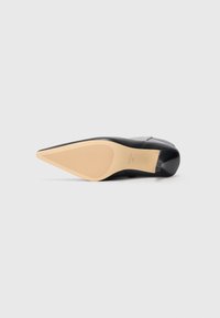 Black leather high heel shoe with a pointed toe. Features a textured beige rubber sole with horizontal grooves for grip.