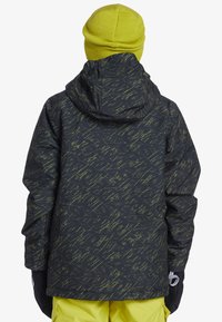 Svart jacka med strukturerat grönt abstrakt mönster, med huva och elastiska mudd, tillsammans med en ljusgul stickad mössa.