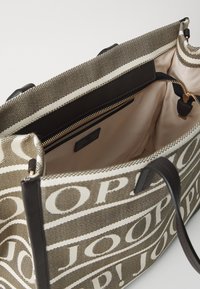 Torba na ramię z płótna w kolorze brązowym i kremowym z wzorem logo "JOOP!", skórzanymi akcentami oraz kieszenią wewnętrzną na zamek. Gładka struktura, przestronny design.
