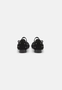 Chaussures en suede noires avec un dos ouvert, ornées de petites clous blancs, et dotées d'un petit talon. Texture lisse et design classique.