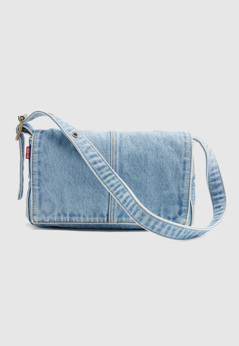 Borsa a tracolla in denim azzurro chiaro con tracolla regolabile e etichetta rossa Levi's sul lato sinistro, su uno sfondo grigio chiaro uniforme.