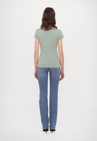 Lichtgroen aansluitend T-shirt met korte mouwen, gedragen met blauwe flared jeans. De outfit heeft een eenvoudig ontwerp en een gladde textuur.