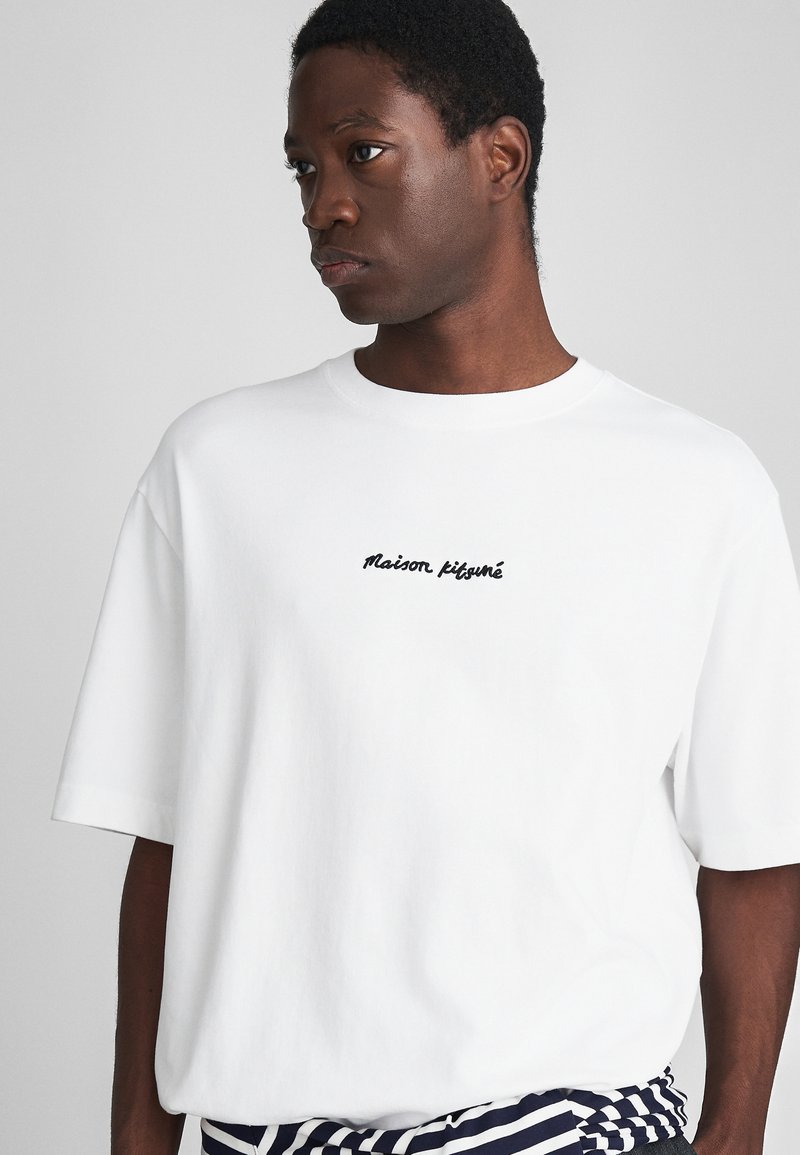 White cotton T-shirt with a round neck, loose fit, and short sleeves; features black embroidered text "Maison Kitsuné" on the front.