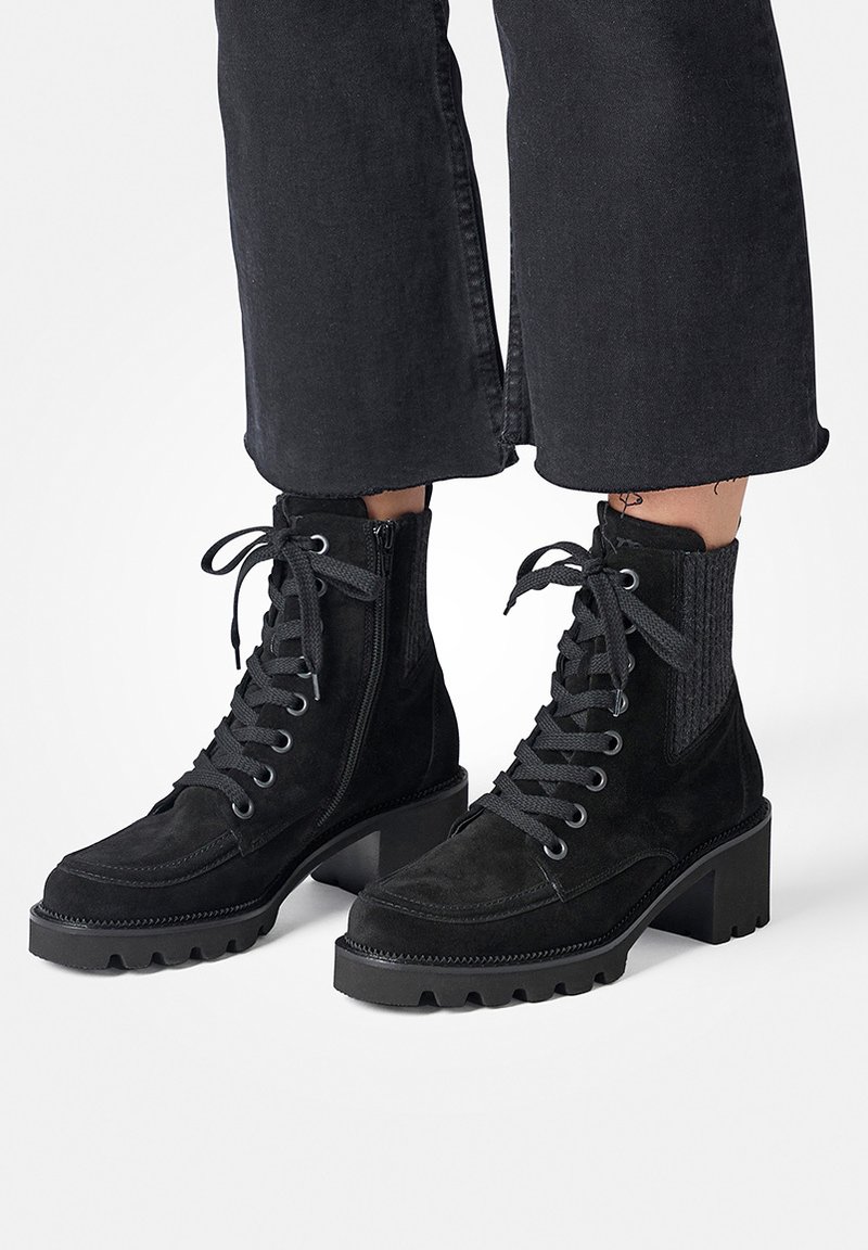 Bottines en suède noir avec un talon épais, fermeture à lacets, fermeture éclair sur le côté, accents côtelés et semelle texturée pour une meilleure adhérence et stabilité.