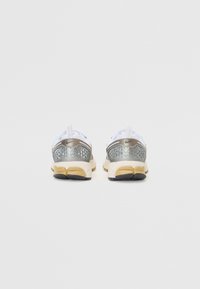 Chaussures de sport blanches avec une tige en maille argentée, présentant un motif texturé et une semelle intermédiaire beige avec une semelle extérieure noire.