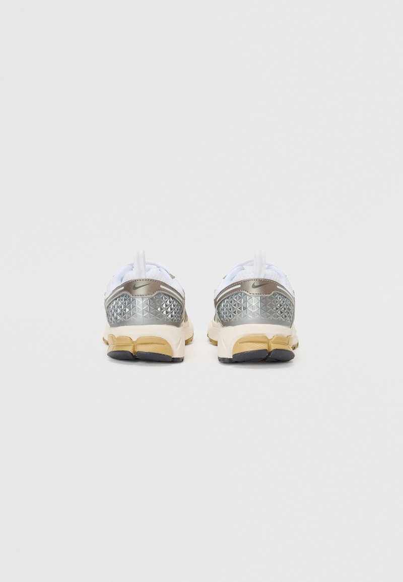 Chaussures de sport blanches avec une tige en maille argentée, présentant un motif texturé et une semelle intermédiaire beige avec une semelle extérieure noire.