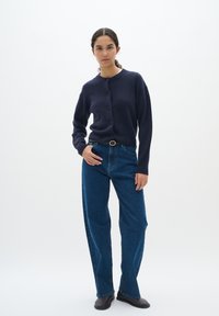 Mörkblå ullcardigan med rund halsringning och knappar, tillsammans med högmidjade blå denimjeans och svarta slip-on skor.