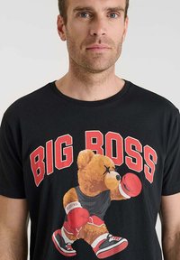 Camiseta negra de manga corta con un gráfico de un oso boxeador, con el texto "BIG BOSS" en rojo arriba. El oso lleva guantes de boxeo rojos y zapatillas.