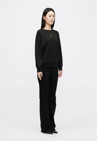 Černý svetr s kulatým výstřihem, volný střih a žebrované manžety. Doplněno černými kalhotami rovného střihu a černými špičatými botami.