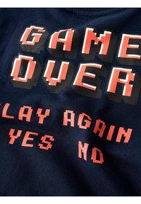 Felpa blu navy con testo pixelato recante la scritta "GAME OVER" in rosso e arancione, con la frase "PLAY AGAIN YES NO" sotto. Tessuto morbido.