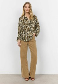 Loose-fitting, long-sleeve blouse with an abstract brown, green, and cream pattern; paired with wide-leg, beige pants and brown sandals.