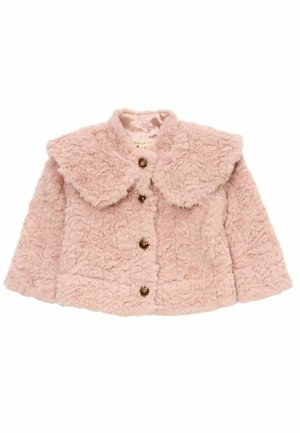 Ung pige iført en lyserød fluffy jakke, blomsterplisseret nederdel og gyldne sko, smilende og stående på en lys baggrund.