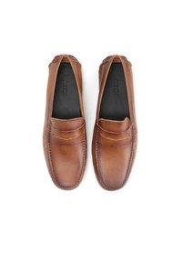 Mocasines de cuero marrón con suela plana, que presentan detalles de costura y una textura suave. El interior es negro y muestra un logo.
