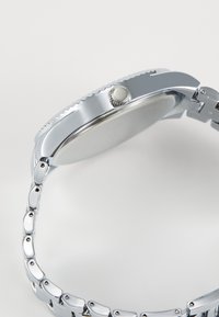 Montre en acier inoxydable argenté avec un boîtier rond, une couronne texturée et un bracelet à maillons avec finition polie.