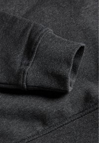 Felpa grigia scura con polsini e orlo a costine, texture morbida e design semplice senza loghi o motivi visibili.