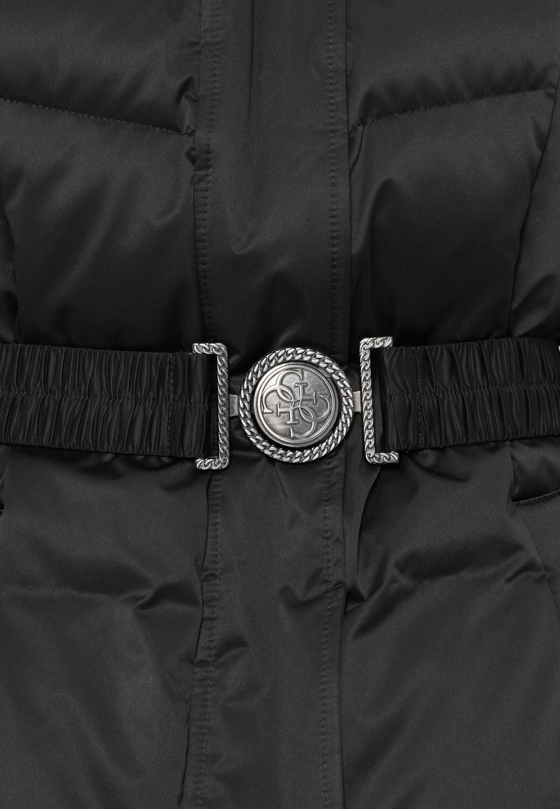 Chaqueta acolchada negra con un cinturón elástico gathered que presenta una hebilla redonda de plata grabada con un logo entrelazado.