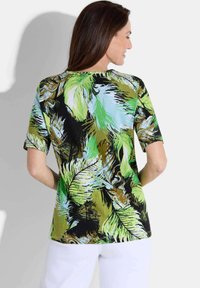 Kurzarmoberteil mit einem lebhaften Muster aus grünen und schwarzen tropischen Blättern, rundem Ausschnitt und lockerer Passform. Hergestellt aus einem glatten Material.