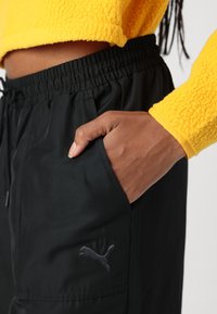 Pantalons de jogging noirs avec ceinture élastique, poches latérales et un petit logo Puma gris. Assortis à un pull court jaune duveteux.