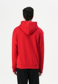 Red hoodie with a kangaroo pocket, ribbed cuffs, and a drawstring hood. The back features a seamless design and soft texture.
