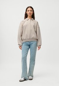 Beige genser med krage, senkede skuldre og ribbestrikket kant. Brukt med lyseblå utsvingte jeans og grå joggesko.