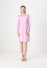 Vestido rosa con una silueta ajustada, escote con bordes en forma de concha y mangas largas con recortes en forma de concha. Tejido suave con una textura delicada.