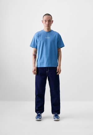 Lyseblå bomulls-T-skjorte med rund hals og korte ermer, kombinert med mørkeblå jeans og blå joggesko.