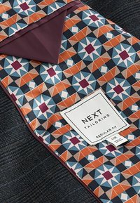 Țesătură personalizată cu un model geometric în nuanțe de albastru, portocaliu și crem. Are o căptușeală violet și o etichetă albă cu informații despre brand.