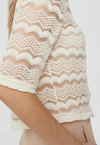 Blommig crop top i off-white med zickzackmönster och en texturerad stickning. Kort ärm med vågig kant och lätt material.