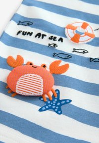 Blau-weiß gestreifter Stoff mit einem Design von einem orangen Krebs und einem Seestern. Mit gestickten Details und dem Text "SPASS AM MEER."