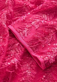 Roze stof met pailletten in gefranjeerde patronen, met een zachte textuur en glanzend oppervlak, waardoor een gelaagde look met diepte ontstaat.