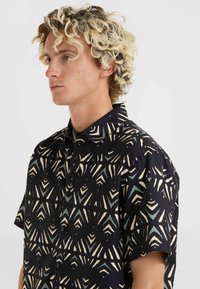 Short-sleeved black shirt featuring a geometric cream and teal pattern, made from a lightweight fabric with a classic collar and button closure.