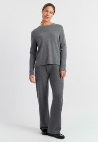 Grijze gebreide trui met ribgebreide manchetten en een ronde hals, gecombineerd met bijpassende brede broekspijpen. Zachte textuur en een ontspannen pasvorm door het geheel.