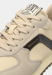 Baskets en daim beige avec un accent en cuir marron foncé, bout rond, surface texturée et lacets beiges. Comprend une étiquette de langue de marque et des coutures.