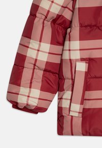 Sezione di giacca puffer a quadri rossi e crema, caratterizzata da una texture trapuntata e una tasca esterna sulla manica, con polsini elasticizzati.