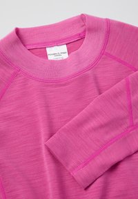 Lähikuva vaaleanpunaisesta pitkähihaisesta paidasta, jossa on näkyviä sauman yksityiskohtia ja etiketti, joka näyttää brändin ja koon kauluksessa.