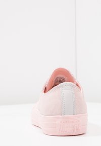 Vaaleanpunaiset mokkanahkakengät, joissa on harmaa kantapää, litteä kumipohja ja painettu "Converse All Star" -logo takana.