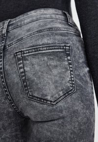 Vaqueros desgastados de un gris oscuro que presentan un bolsillo trasero con costuras contrastantes y una textura ligeramente deslavada.