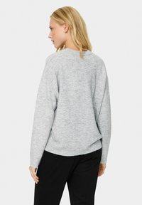 Jasnoszary sweter robiony na drutach o luźnym kroju, z prążkowanym dołem i detalem szwu z tyłu. Posiada długie rękawy oraz gładką, miękką teksturę.