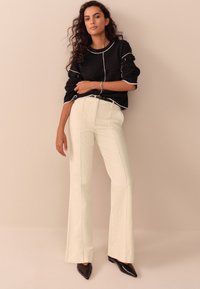 Maglione nero con cuciture bianche, abbinato a pantaloni bianchi svasati a vita alta e scarpe nere a punta. Design minimalista e linee pulite.