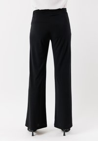 Pantaloni neri a gamba larga con una texture liscia, vita elastica e vestibilità sartoriale. L'orlo termina appena sopra le scarpe.