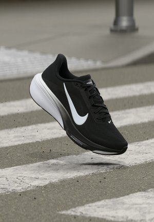 Μονόχρωμο μαύρο και λευκό παπούτσι Nike για τρέξιμο στον αέρα πάνω από διάβαση πεζών σε ασφάλτινο δρόμο.