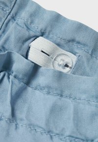 Tela azul claro con una textura suave, que presenta una cinturilla elástica blanca y un detalle de botón transparente cerca del borde superior.
