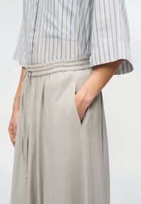Pantalon gris clair à jambes larges avec taille élastique, doté de poches latérales. Assorti à une chemise grise rayée boutonnée. Texture lisse.