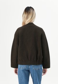 Brun oversized genser med teksturert finish, ribbestrikket kant og avslappede ermer, kombinert med lyseblå denimjeans.
