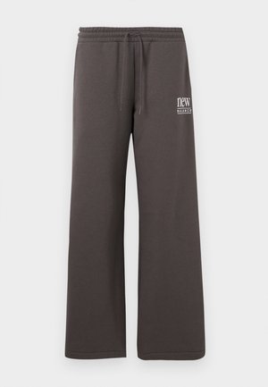 Pantalones deportivos anchos de color gris oscuro con cintura elástica, cordón y logo blanco de "new balance" en el muslo izquierdo.