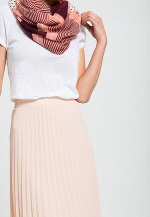 Femme portant un haut blanc à manches courtes, une jupe plissée rose clair et une écharpe rose et bordeaux à motifs multiples autour du cou.