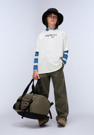 Olive green duffel bag with black accents. Model wears a white shirt with "Napapijri 1987" text, blue and white striped long sleeves, and green pants.