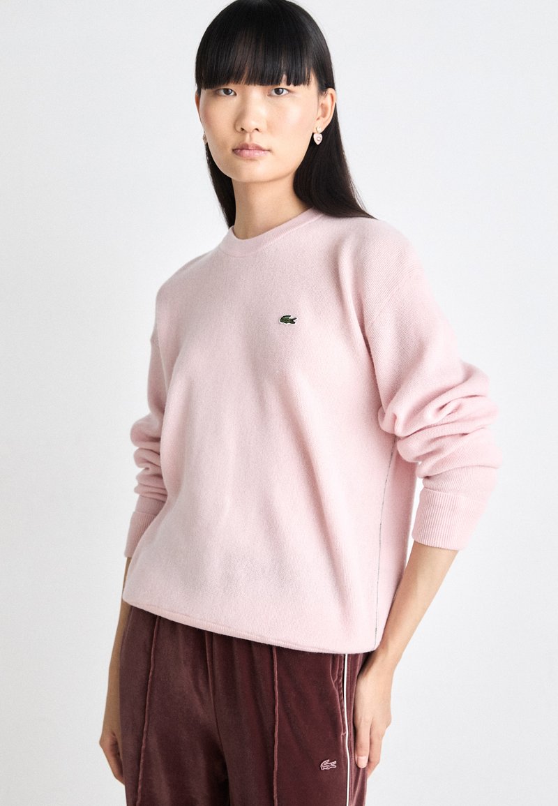 Helles rosa Sweatshirt aus weichem Stoff, mit Rundhalsausschnitt, gerippten Bündchen und einem kleinen grünen Lacoste-Logo auf der Brust.